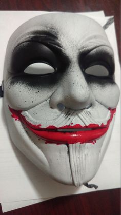 a white mask with black and red paint on it, sitting on top of a piece of paper