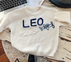 a sweater with the word leo written on it sitting next to a laptop and keyboard