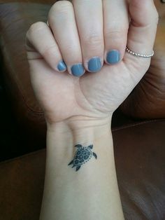 a woman's hand with a small turtle tattoo on her left wrist and blue nail polish