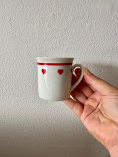 a hand holding a coffee cup with hearts painted on the side and red trim around the edge