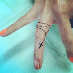 a person's hand with a small cross tattoo on the middle finger and an orange nail