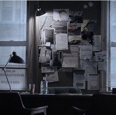 a room with several papers on the wall and a desk in front of two windows