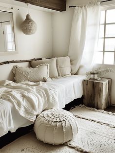 a white bed sitting in a bedroom next to a window with curtains and pillows on top of it