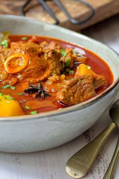 a bowl of stew with meat and vegetables in it on a table next to silverware