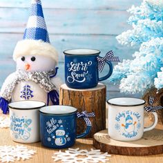 coffee mugs with snowmen on them are sitting next to a tree and blue christmas decorations