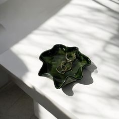 a green bowl sitting on top of a white table next to a wall with two gold rings in it