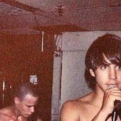 two shirtless men singing into microphones in a room