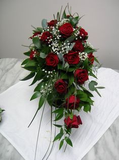 a bouquet of red roses and baby's breath on a white cloth with greenery