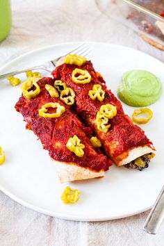 two pieces of pizza on a white plate with green sauce and silverware next to it