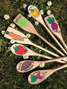 six wooden spoons with vegetables on them sitting in the grass next to daisies