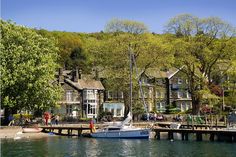 a sailboat is docked in the water next to a large house and tree covered hill