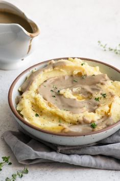 a bowl filled with mashed potatoes and gravy on top of a table