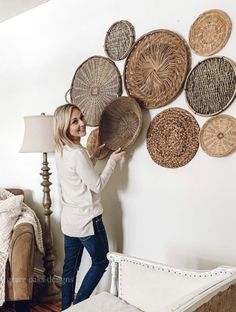 a woman standing next to a wall with woven baskets on it's head and one hand