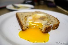 an egg is in the middle of toast on a white plate with yellow liquid coming out of it