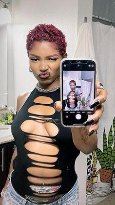 a woman taking a selfie with her cell phone in front of her face and showing off the cutouts on her shirt