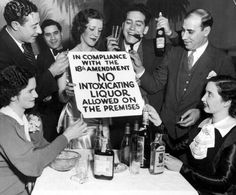 a group of people standing around a table holding up signs and drinking alcohol in front of them