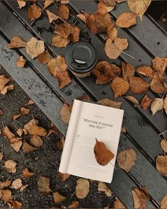 an open book sitting on top of a wooden bench next to leaves and a coffee cup