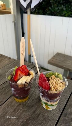 two cups filled with fruit and granola on top of a wooden table