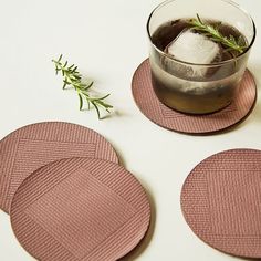 three pink coasters on a white table with a drink and rosemary sprig