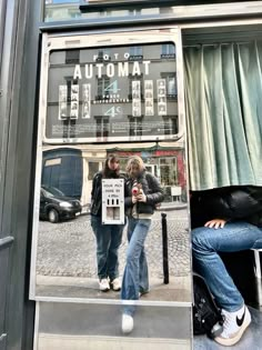 two people sitting on a bench in front of a bus window with an automat sign