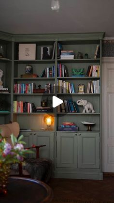 a living room filled with lots of books on top of green bookcases next to a doorway