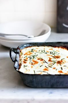 a casserole dish with cheese and herbs in it sitting on a kitchen counter