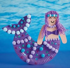 a purple paper plate with a mermaid on it and pom poms around her hair