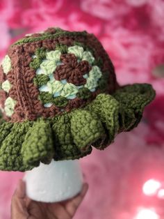 a crocheted hat is being held up by someone's hand in front of a pink background