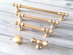 four brass handles and knobs on a white wooden surface with measurements for each handle