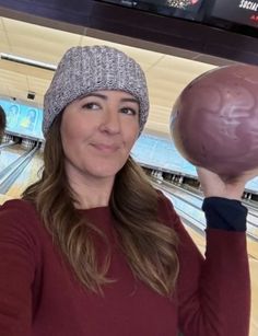 a woman holding up a chocolate doughnut in front of her face at a bowling alley