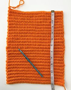 an orange crochet square with a needle and measuring tape