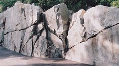 a large rock wall in the middle of a road with trees and bushes behind it