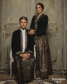 two people are sitting on a chair in front of a wall with an ornate pattern