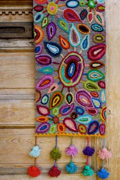 a colorful wall hanging made out of felt and yarn with tassels on it