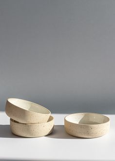 two white bowls sitting next to each other on top of a table with grey walls in the background