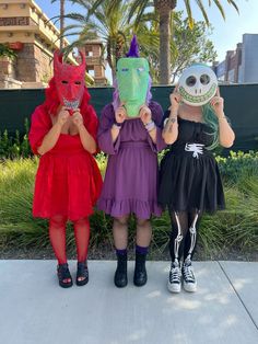 three girls in costumes are holding up masks