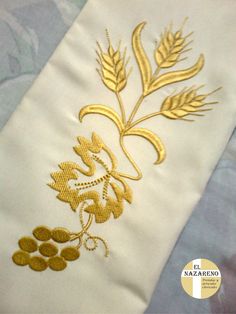 a close up of a white cloth with gold embroidery on it and grapes in the center