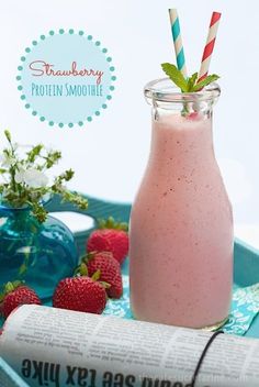 a strawberry milkshake in a glass with strawberries next to it on a blue tray