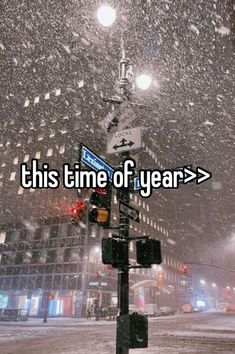 a street light with the words this time of year on it in front of a snowy cityscape