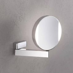 a round mirror mounted to the side of a white wall next to a metal shelf