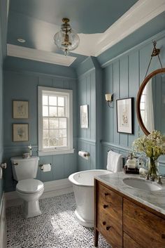 a bathroom with blue walls, white fixtures and a large round mirror above the bathtub