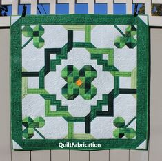 a green and white quilted wall hanging on the side of a fence with text overlay that says quiltfabrication