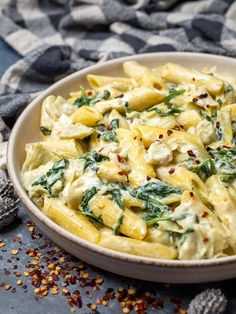 a white bowl filled with pasta and spinach on top of a blue table cloth