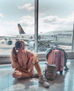 a woman sitting on the ground next to her luggage and looking out an airport window