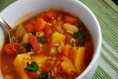 a white bowl filled with vegetable soup on top of a green table cloth next to a spoon