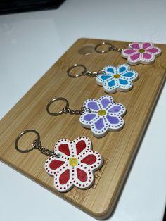 four flower shaped key chains sitting on top of a wooden cutting board next to each other