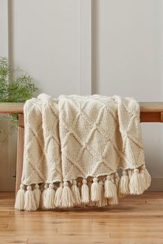 a white blanket sitting on top of a wooden bench next to a potted plant