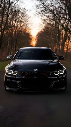 the front end of a black bmw car on a road with trees in the background