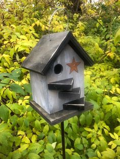 a bird house sitting on top of a metal pole next to green bushes and trees