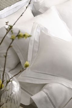 white sheets and pillows are piled on top of each other with yellow flowers in the foreground